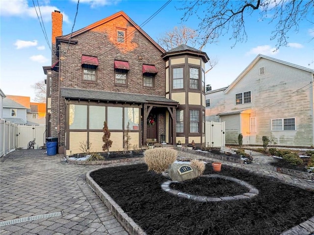 view of front of property with brick siding, a chimney, fence, and a gate