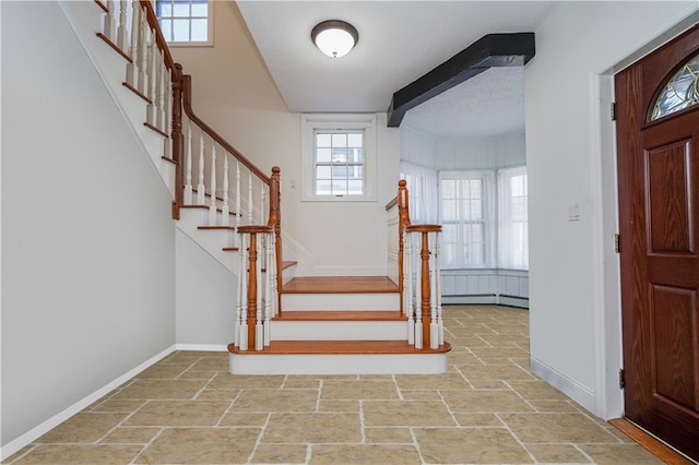 entrance foyer featuring a wealth of natural light, a baseboard heating unit, baseboards, and stone tile floors