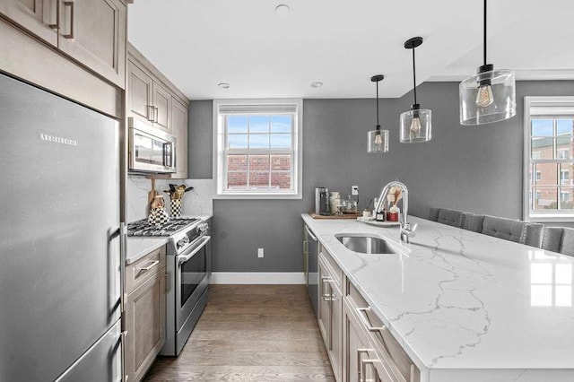 kitchen with sink, high end appliances, wood-type flooring, light stone countertops, and decorative light fixtures