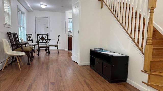 corridor with a baseboard heating unit, stairs, baseboards, and wood finished floors