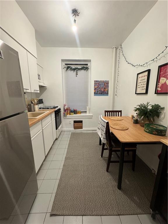 kitchen with range with gas cooktop, stainless steel refrigerator, white cabinets, and light tile patterned flooring