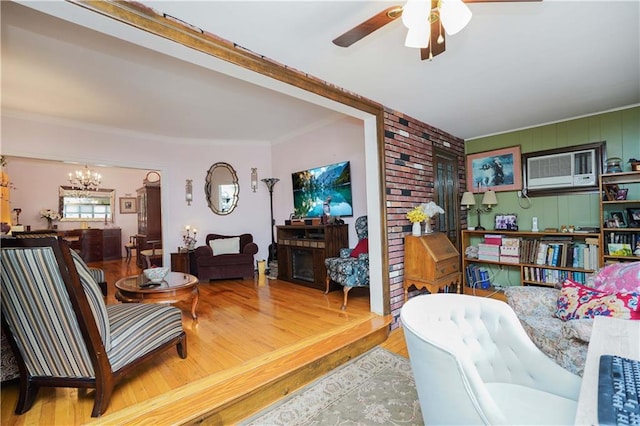 living room with ornamental molding, ceiling fan with notable chandelier, a wall mounted air conditioner, and wood finished floors