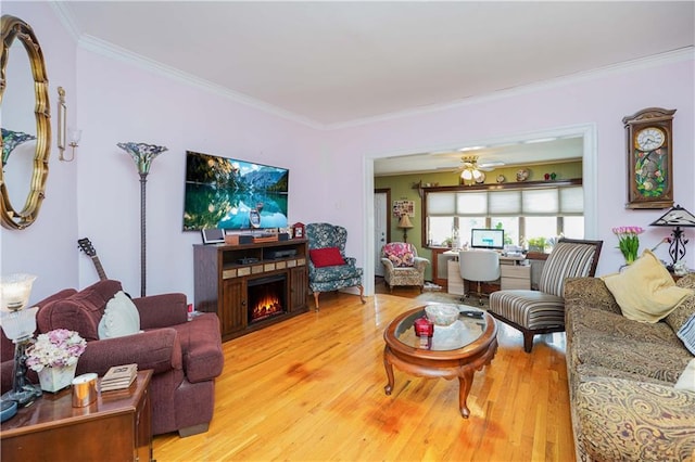 living room with a lit fireplace, crown molding, a ceiling fan, and wood finished floors