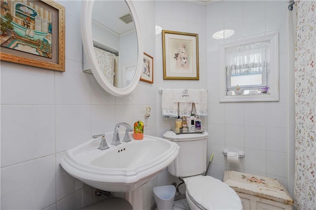 bathroom featuring walk in shower, toilet, sink, tile walls, and ornamental molding