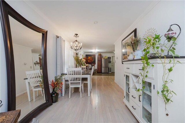 hallway with an inviting chandelier, crown molding, and light wood-type flooring