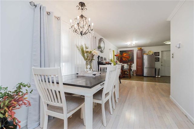 dining area featuring baseboards, ornamental molding, an inviting chandelier, and light wood-style floors