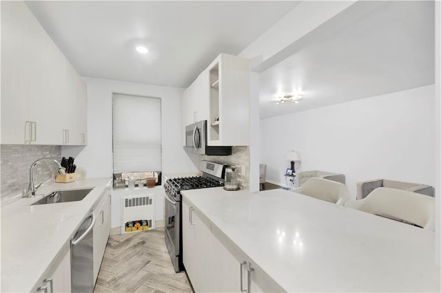 kitchen with appliances with stainless steel finishes, radiator heating unit, white cabinetry, sink, and light parquet floors