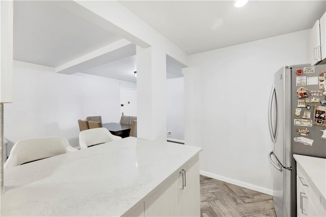 kitchen featuring white cabinetry, stainless steel fridge, light stone counters, and light parquet floors