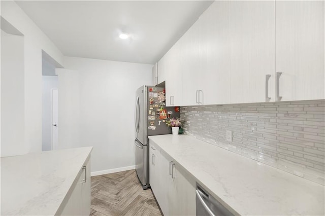 kitchen featuring tasteful backsplash, light stone counters, stainless steel fridge, light parquet flooring, and white cabinets