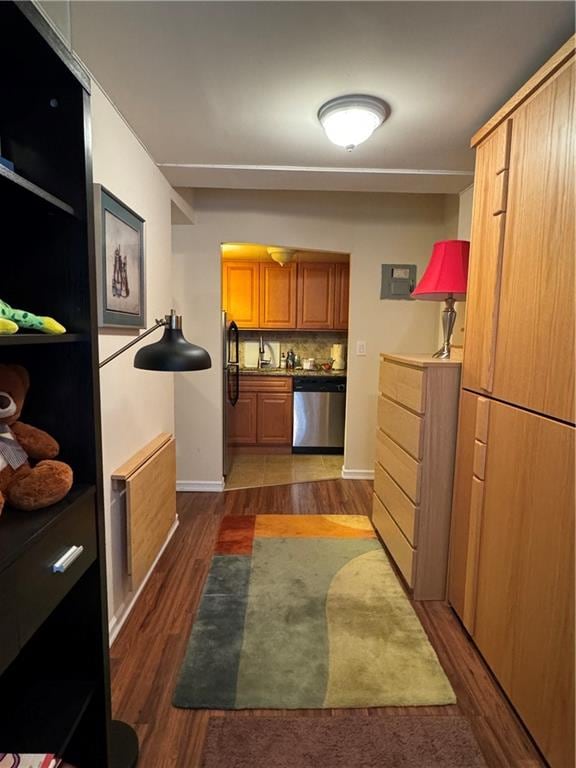 kitchen featuring brown cabinets, dark wood-type flooring, stainless steel dishwasher, tasteful backsplash, and freestanding refrigerator