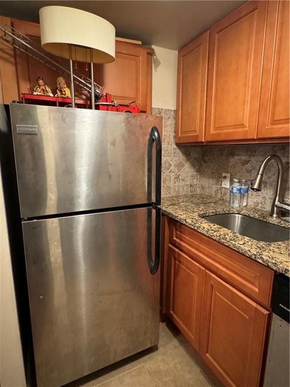 kitchen with light stone countertops, a sink, stainless steel appliances, brown cabinets, and backsplash