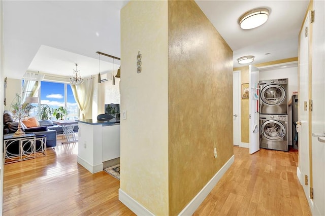 hall featuring stacked washer and dryer, a wall mounted AC, a notable chandelier, and light wood-type flooring