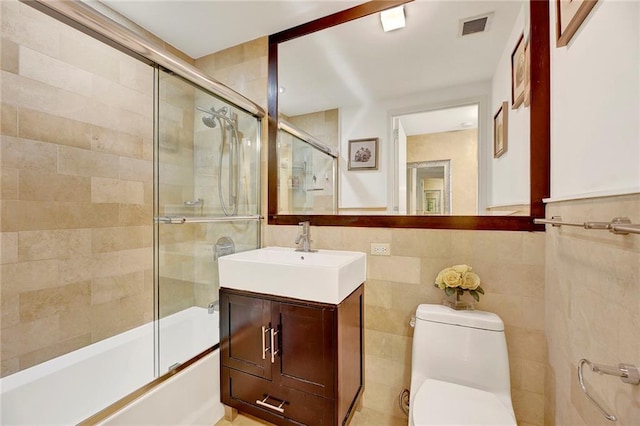 full bath featuring tile walls, bath / shower combo with glass door, visible vents, toilet, and vanity