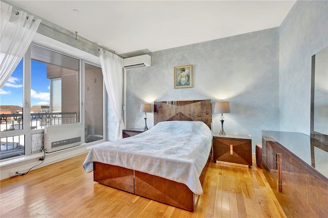 bedroom featuring a wall mounted air conditioner, light wood-style flooring, and access to exterior