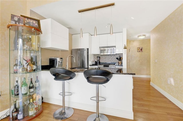 kitchen with white cabinetry, light wood-type flooring, appliances with stainless steel finishes, a kitchen breakfast bar, and dark stone counters