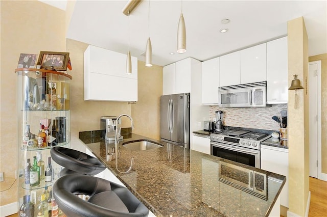 kitchen with hanging light fixtures, appliances with stainless steel finishes, white cabinetry, a sink, and dark stone counters