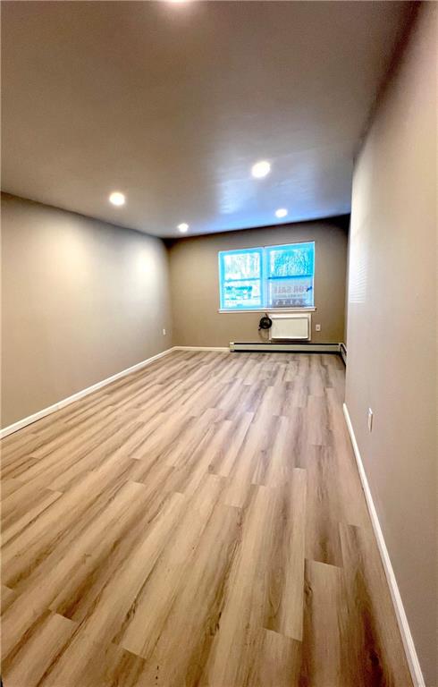 basement featuring light hardwood / wood-style flooring and a baseboard heating unit