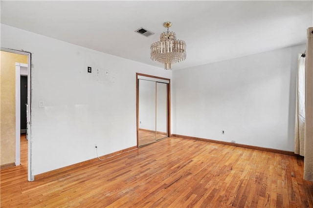 empty room with a notable chandelier and light wood-type flooring