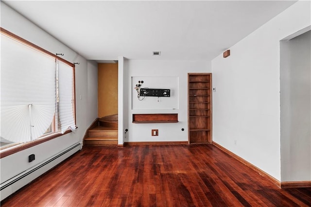 unfurnished room with built in shelves, dark wood-type flooring, and a baseboard heating unit