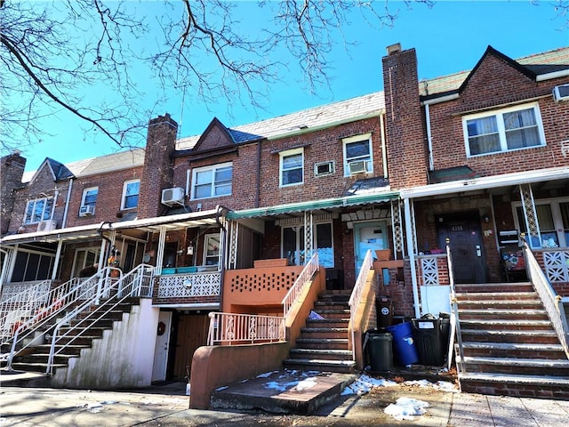 townhome / multi-family property with a high end roof, covered porch, a chimney, stairs, and brick siding