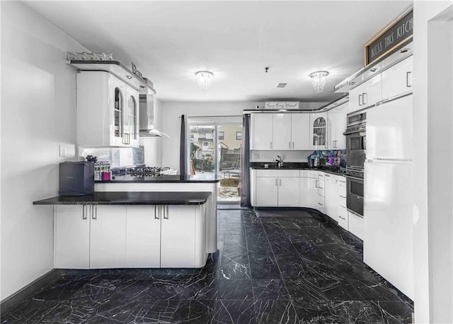 kitchen featuring sink, wall chimney range hood, white cabinetry, white refrigerator, and kitchen peninsula