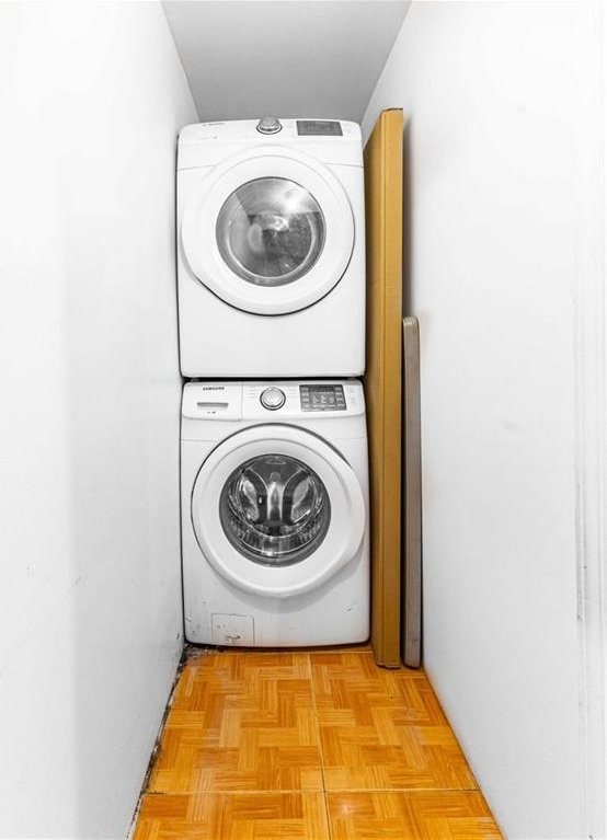 laundry room with light parquet flooring and stacked washer / dryer