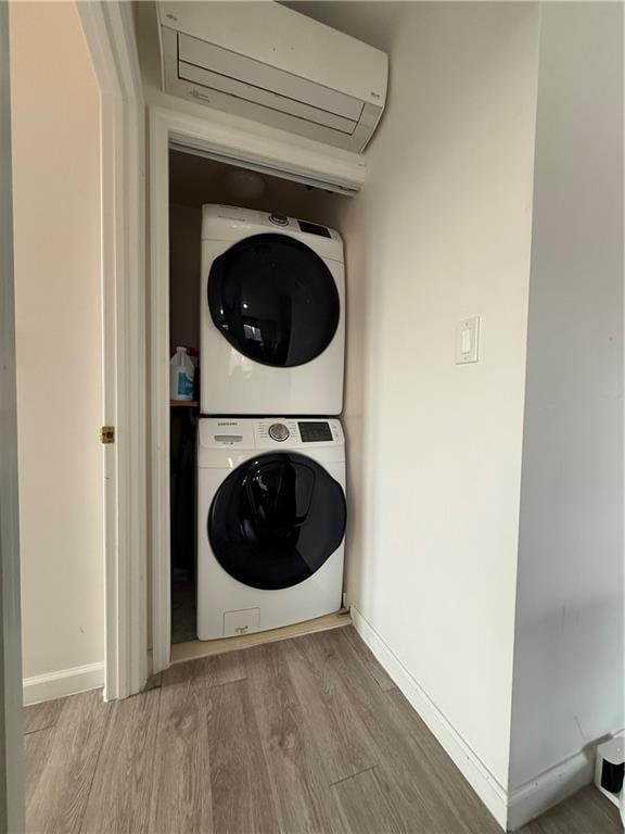 clothes washing area with wood finished floors, stacked washer / dryer, laundry area, and a wall unit AC