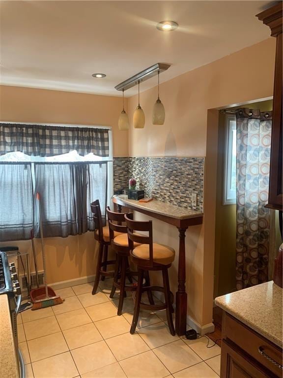 interior space with pendant lighting, light tile patterned flooring, light stone counters, and backsplash