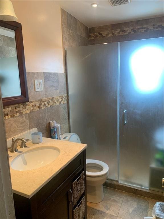 bathroom featuring a shower with door, vanity, tile walls, and toilet