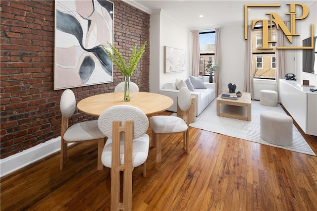 dining area with hardwood / wood-style flooring, ornamental molding, and brick wall