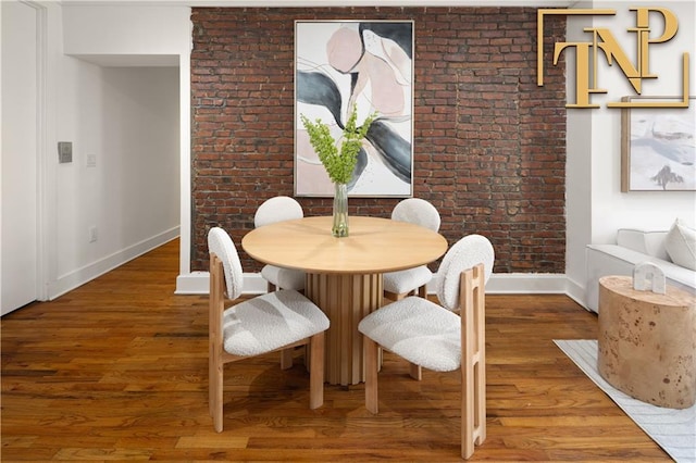 dining area with wood finished floors, baseboards, and brick wall