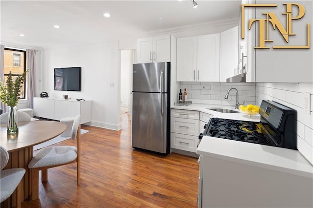 kitchen with backsplash, light countertops, gas range oven, freestanding refrigerator, and a sink