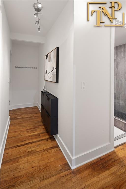 hall featuring track lighting, wood finished floors, and baseboards