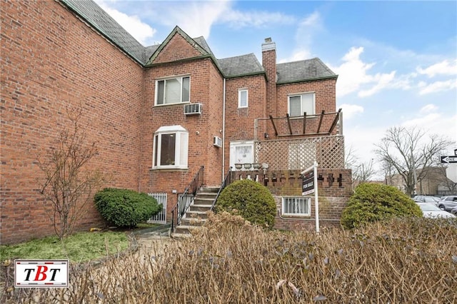 rear view of house featuring a wall unit AC, a chimney, a balcony, brick siding, and stairs