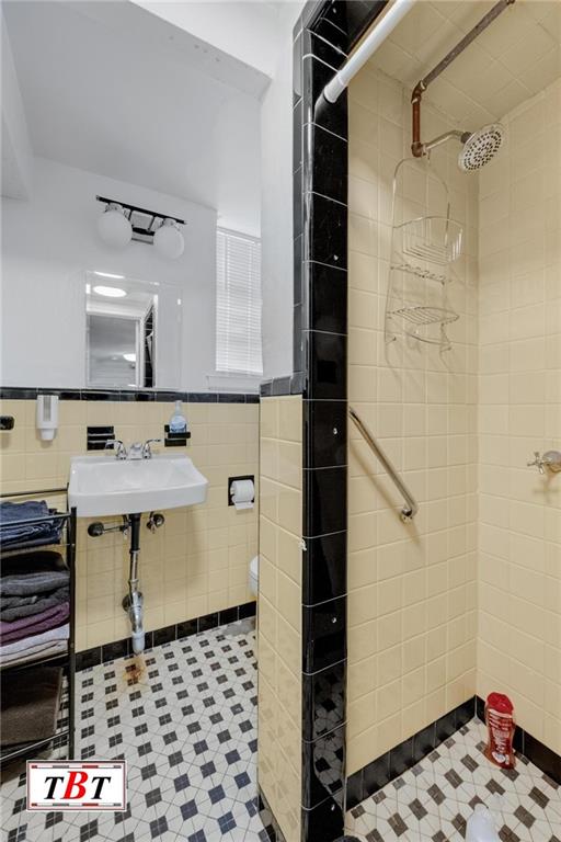 full bath with a stall shower, wainscoting, a sink, and tile walls