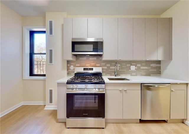 kitchen with appliances with stainless steel finishes, a sink, light wood-style floors, light countertops, and tasteful backsplash
