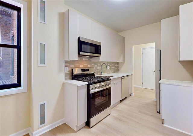 kitchen with sink, white cabinets, decorative backsplash, stainless steel appliances, and light hardwood / wood-style flooring