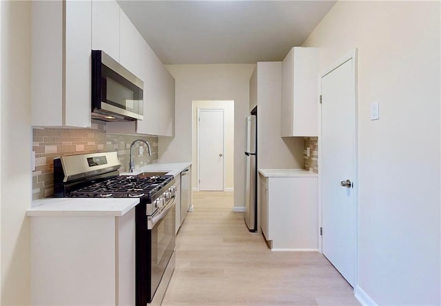 kitchen featuring sink, white cabinetry, tasteful backsplash, light wood-type flooring, and appliances with stainless steel finishes