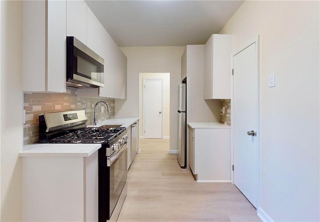 kitchen with appliances with stainless steel finishes, a sink, light wood-style floors, white cabinetry, and backsplash