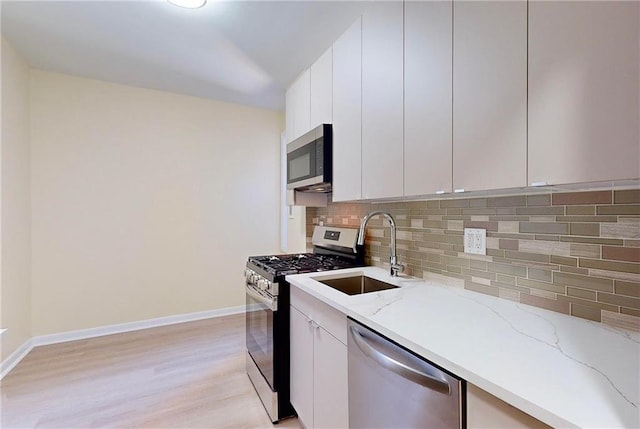 kitchen with sink, white cabinets, stainless steel appliances, light stone countertops, and backsplash