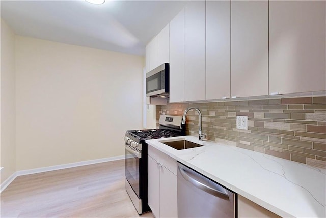 kitchen with tasteful backsplash, a sink, white cabinets, light wood finished floors, and stainless steel appliances