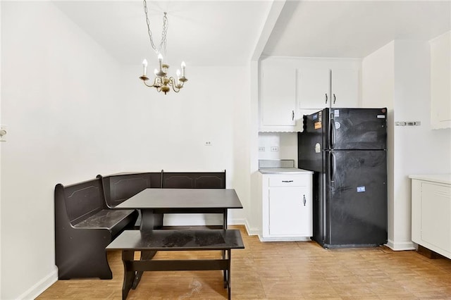 kitchen featuring freestanding refrigerator, white cabinets, a notable chandelier, and baseboards