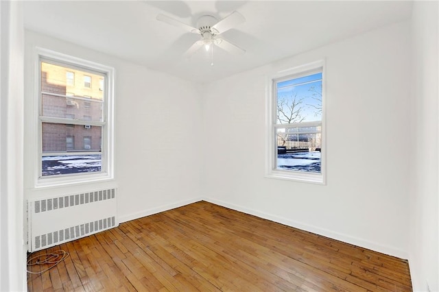 unfurnished room featuring radiator, hardwood / wood-style floors, ceiling fan, and baseboards