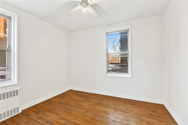 empty room with hardwood / wood-style flooring, radiator heating unit, baseboards, and a ceiling fan