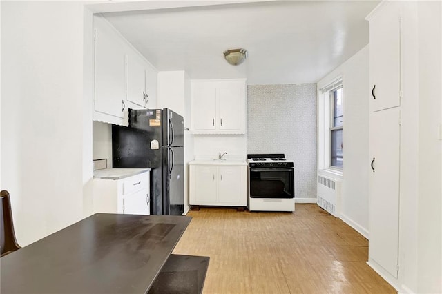 kitchen featuring black fridge, radiator heating unit, range with gas stovetop, and white cabinets