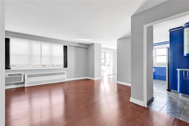 unfurnished living room featuring dark hardwood / wood-style floors, radiator heating unit, and a wall unit AC