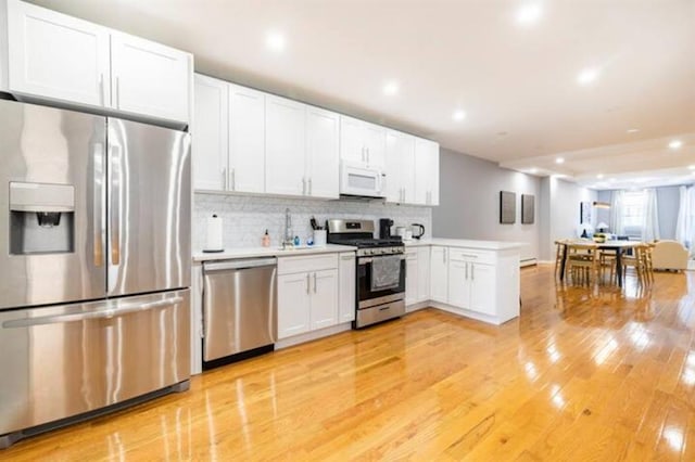 kitchen with light wood-type flooring, kitchen peninsula, white cabinets, stainless steel appliances, and backsplash