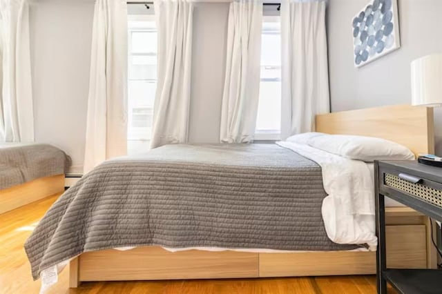 bedroom with multiple windows, hardwood / wood-style flooring, and baseboard heating