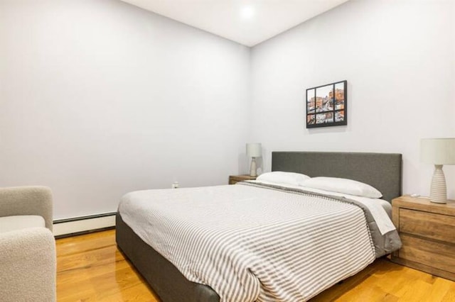 bedroom with a baseboard heating unit and wood-type flooring