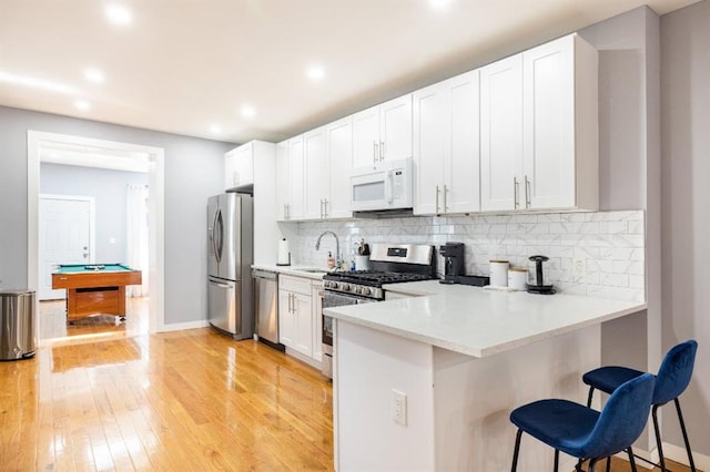 kitchen featuring appliances with stainless steel finishes, a breakfast bar area, white cabinets, decorative backsplash, and light wood-type flooring